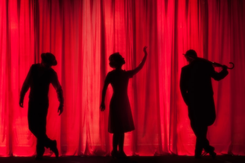 Performer silhouettes against a vivid red theatre curtain
